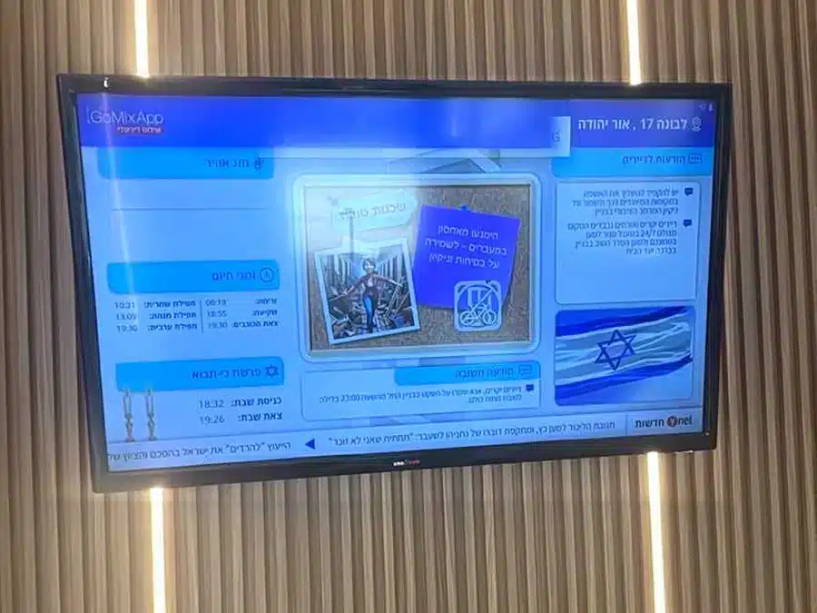 לוח מודעות דיגיטלי לבניין משותף בלבונה 17 אור יהודה — הודעות ועד הבית, זמני היום ופרשת השבוע על מסך בלובי המחופה עץ