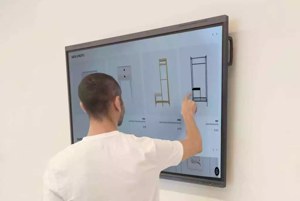 Man interacts with a large interactive digital display showcasing furniture options for purchase.