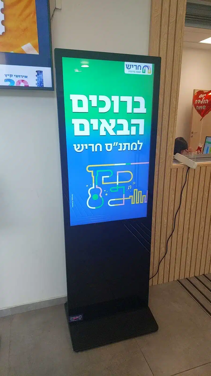 קיוסק רצפתי עם מסך עומד מותקן במתנ״ס חריש — מסך קבלת פנים אנכי בכניסה